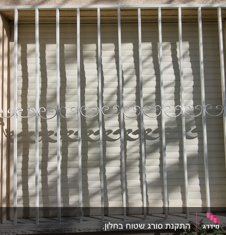 סורגי מתכת לבנים על חלון עם תריס סגור